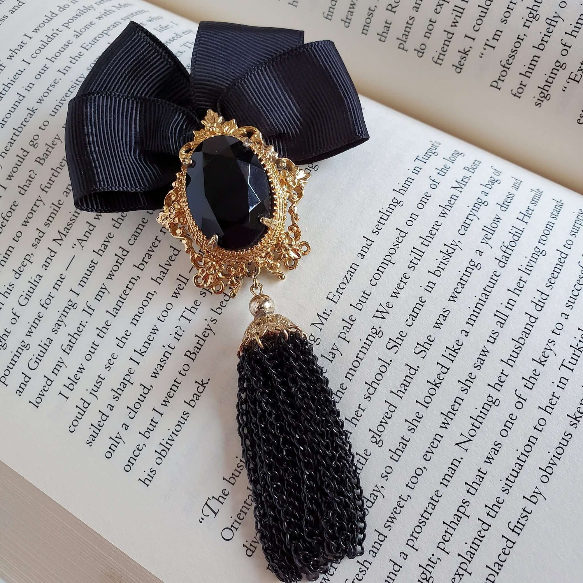 Black ribbon bow brooch with a black stone in a gold setting , and finished with a black tassel