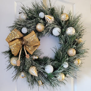 Iced Pine Branches Circle the Wreath. The wreath is decorated with a collection of gold and white sparkling ornaments.