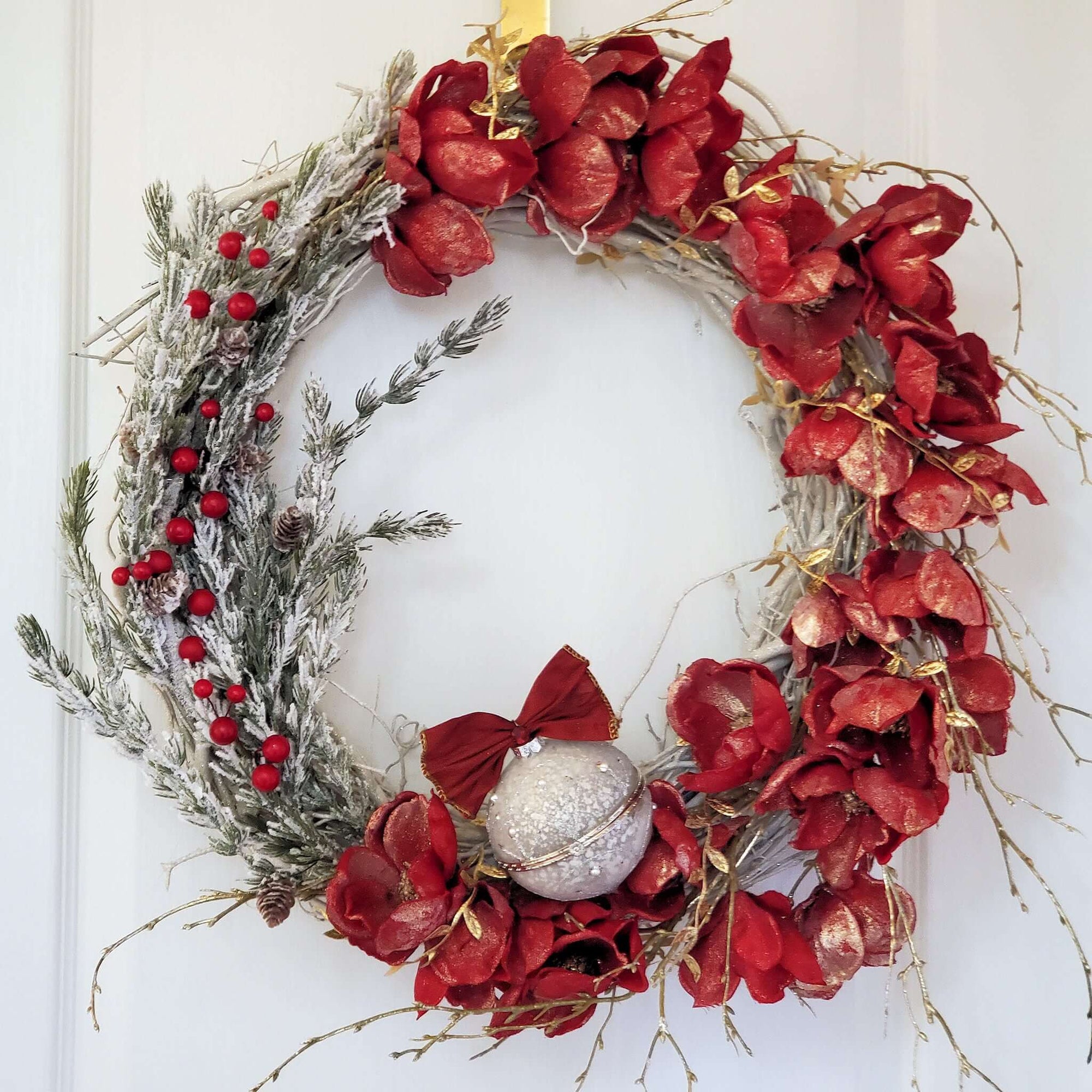 White Grapevine Wreath decorated with red, gold bushed magnolia flowers and a snow dusted pine bough with tiny pine cones and bright red berries.