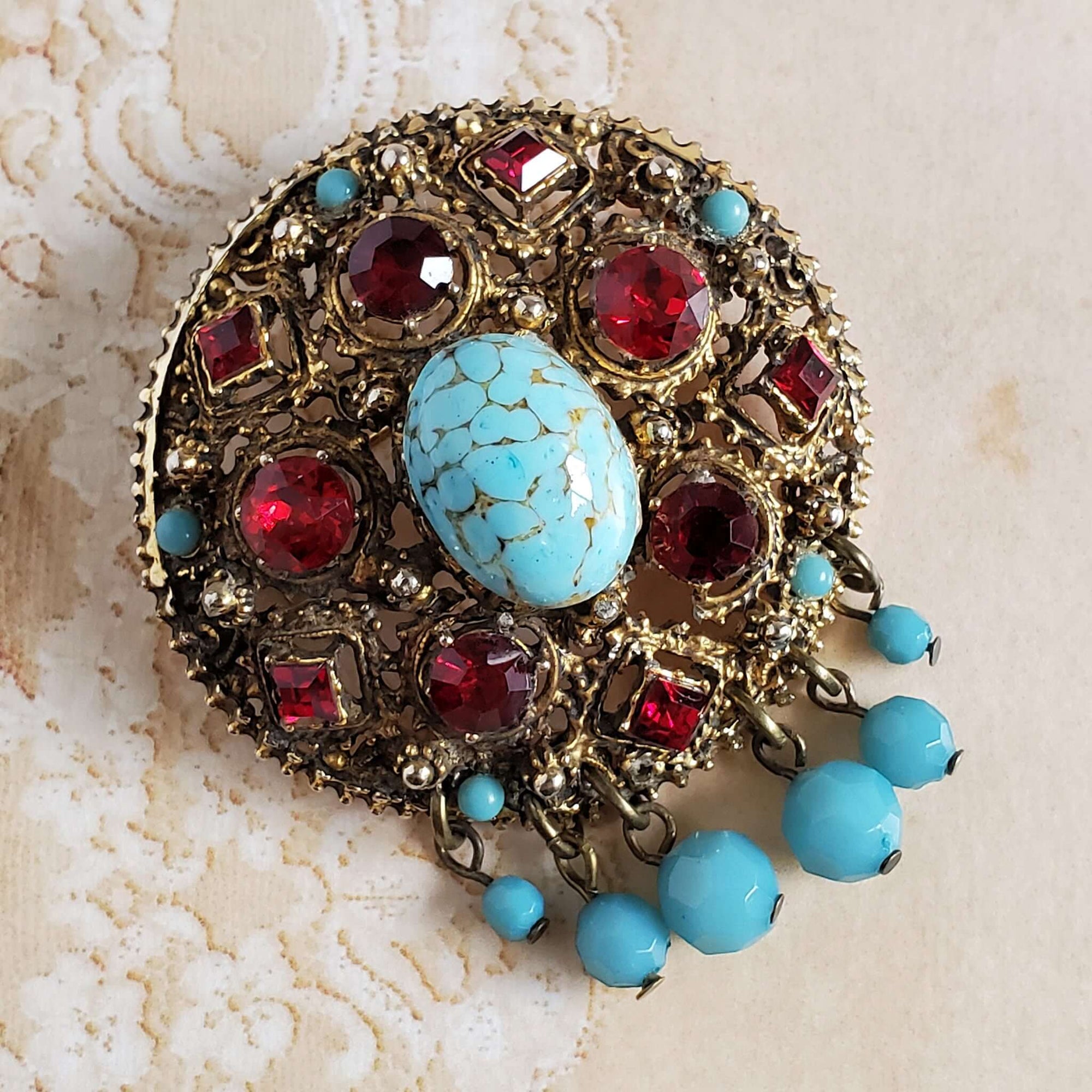 Large Round Antiqued Gold-tone Round Pin with Red Rhinestones and an Imitation Turquoise Center Stone. Turquoise blue beads accent the brooch