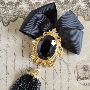 Close up image of the black stone centerpiece, set in a gold filigree setting with a pin backing.