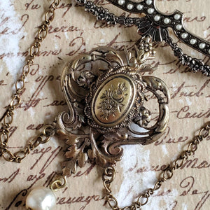 Vintage Victorian style brooch with a swirling leaf and floral design pendant. Suspended from a vintage bar pin that is accented with a floral garland and petite costume pearls . Finished with vintage chain strands and a vintage pearl.